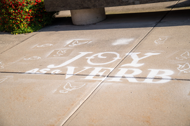 Owens students, faculty and staff were invited to use spray chalk paint to stencil doves around the words "Joy as a Verb" during the Project HOPE public art project.