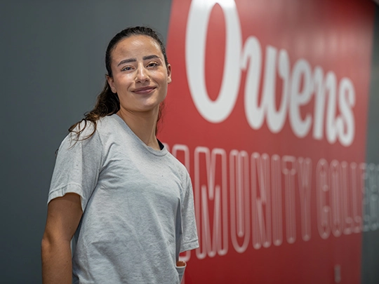 Owens student in front of Owens CC wall design