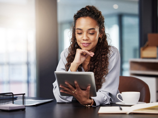 Woman sitting at a desk looking at a tablet smiling