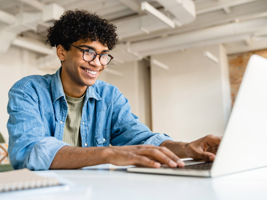 Man sitting at desk with a laptop looking at the screen smiling