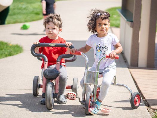 Two children riding toy bikes outside playing
