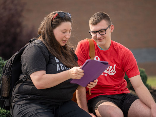 Two students looking at a tablet sitting on a bench