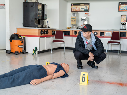 Law enforcement student kneeling down looking at a mannequin for a mock crime scene