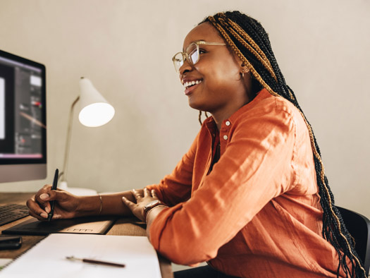 Woman sitting at a desk looking at a computer, writing information down