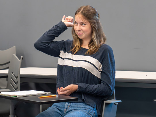 Girl sitting down practicing sign language in a classroom