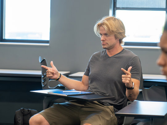 Student sitting at a desk in a classroom practicing sign language