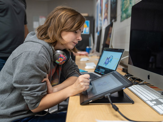 Woman student sitting at a desk animating something on a tablet with a pen