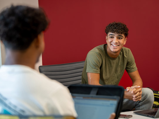 Photo of a student looking at another who is on his computer