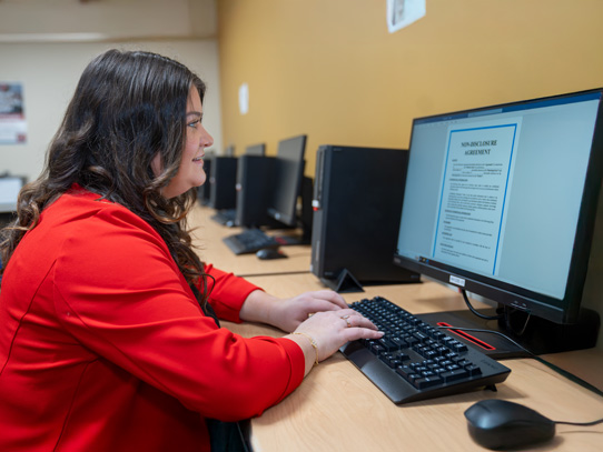 Woman in red sweater at desk typing into a computer