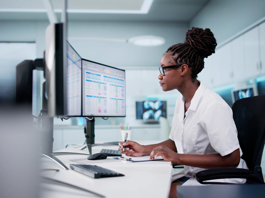 woman in office setting writing while looking at computer screen